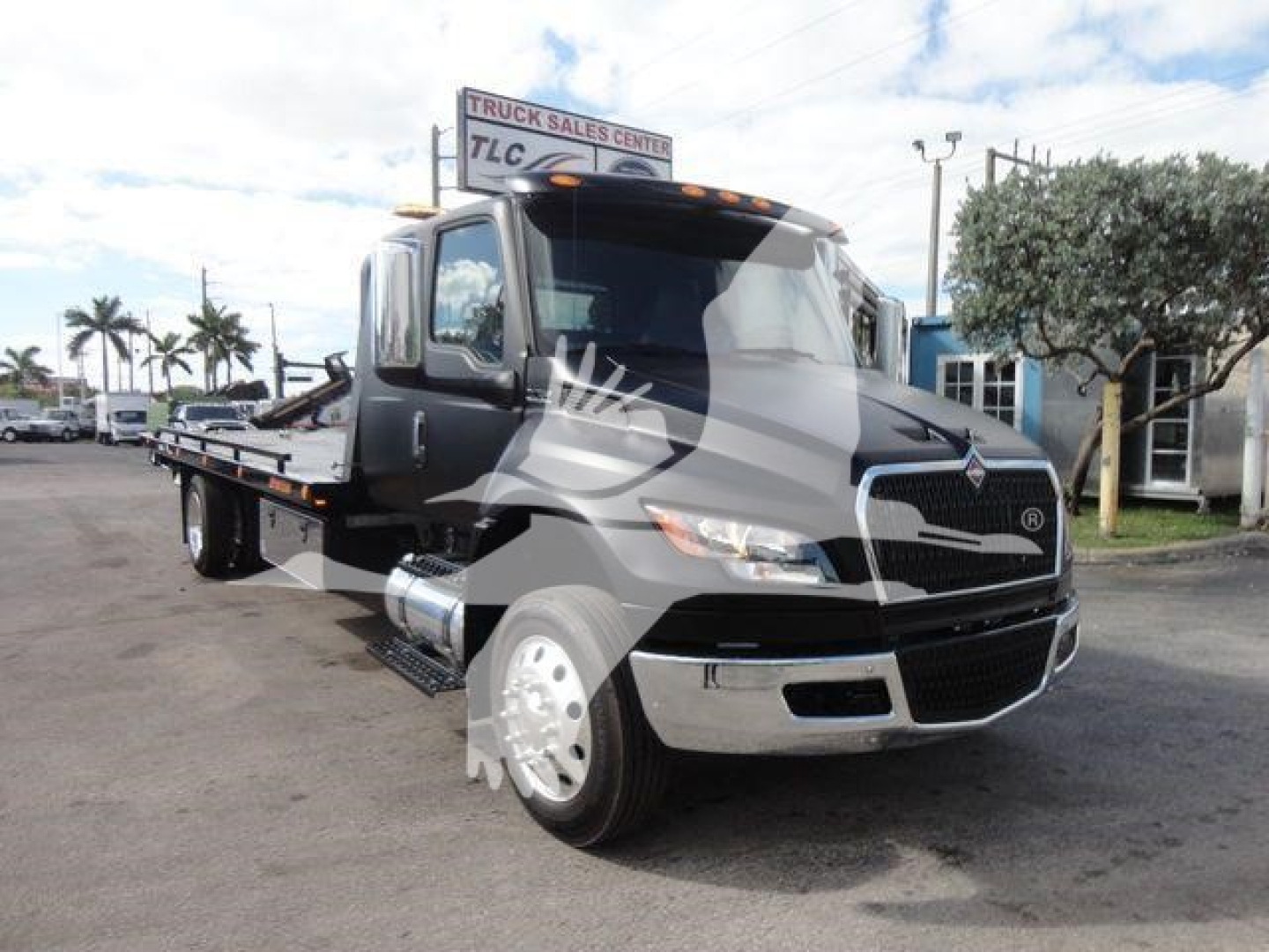 International MV tow truck on a dealership lot, cab view with flatbed. Visible text includes International logo on grille and chrome bumper.