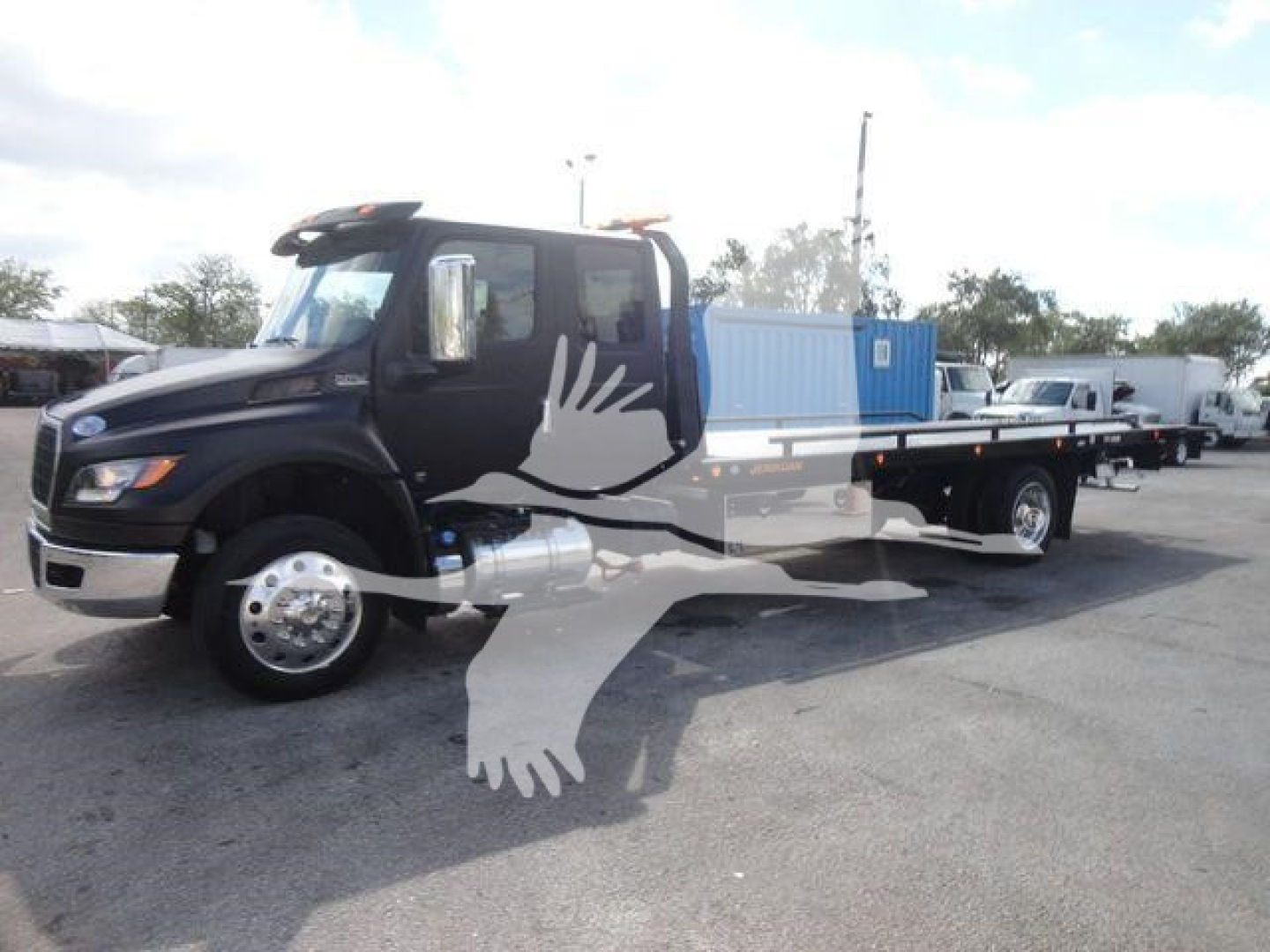 Heavy tow truck with black cab and flatbed, truck and other equipment in background; watermark of a flying eagle silhouette overlaying image.