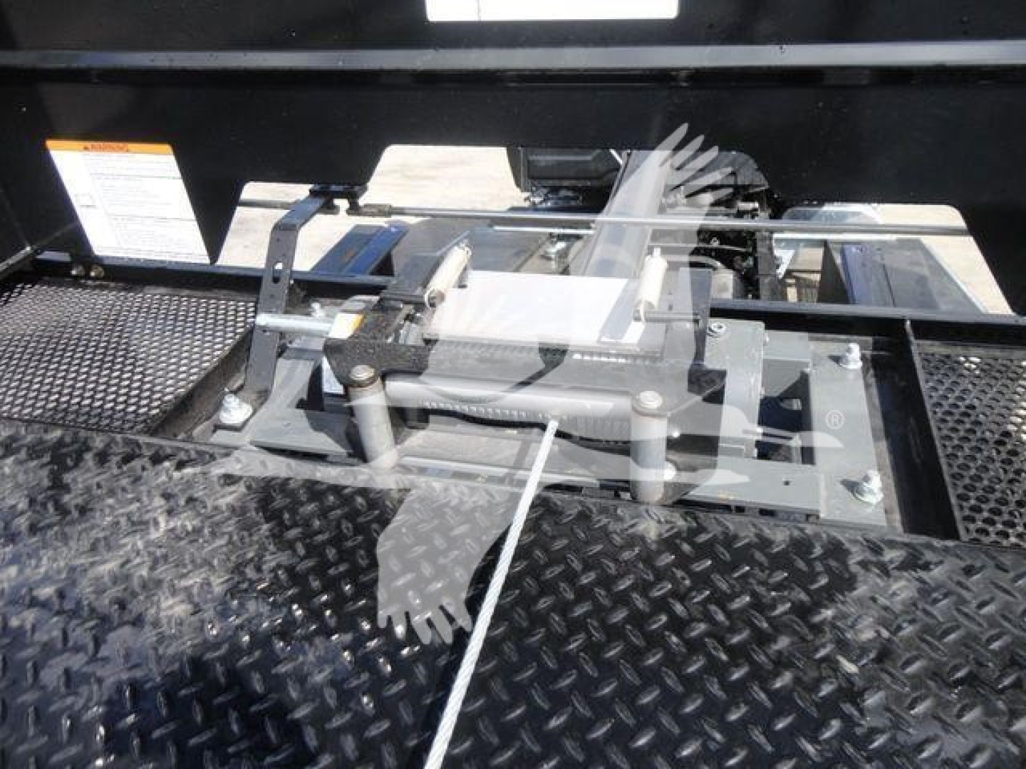 Truck bed area with hydraulic winch and gear mechanism, metal diamond plate surface, cables and levers visible.