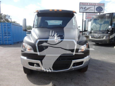 Front view of a 2027 International MV rollback truck with large grille, chrome bumper, and header lights. Signs in background indicate Truck Sales Center.