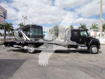 Truck with rollback tow bed and a large black service cab, International MV model, new condition, side view.