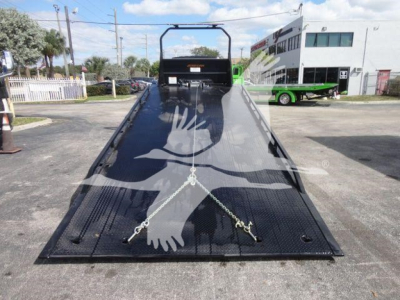Truck towbed with ramp, black metal surface, safety chains, and hook points, in a dealership lot.