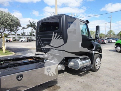 Truck cab side view showing MV Series International rollback truck with large chrome fuel tanks and black exterior.