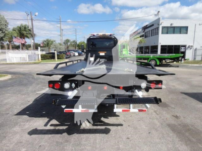 Tractor trailer rollback bed viewed from rear showing flatbed hydraulic ramps and taillights.