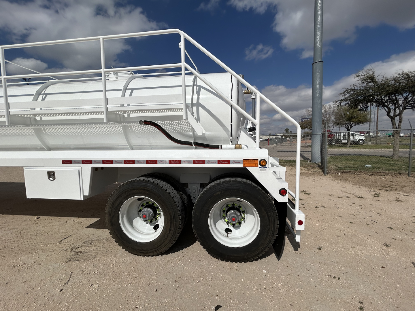 Trailer side view showing dual rear axles and white cylindrical tank with railing and ladder, part of a 2027 Dragon 130BBL vacuum trailer.