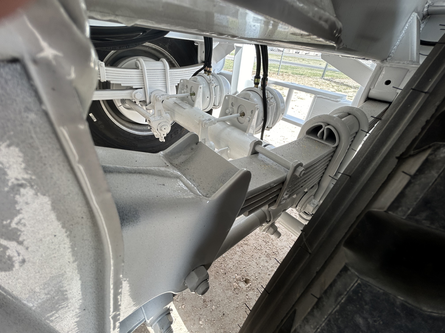 Trailer hitch and suspension components visible under a Dragon 130BBL trailer frame, showing steel axles, leaf springs, and housing with metallic finish.