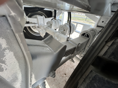 Trailer hitch and suspension components visible under a Dragon 130BBL trailer frame, showing steel axles, leaf springs, and housing with metallic finish.