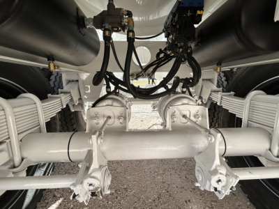 Trailer undercarriage showing axles, suspension, and hydraulic lines; no legible text visible on components.