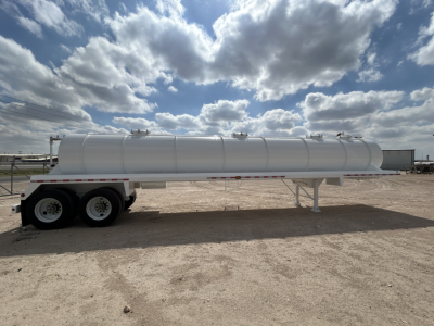 Trailer-mounted vacuum tanker cylindrical tank on dual-axle trailer, white finish, side view with support legs, bright sky with clouds.
