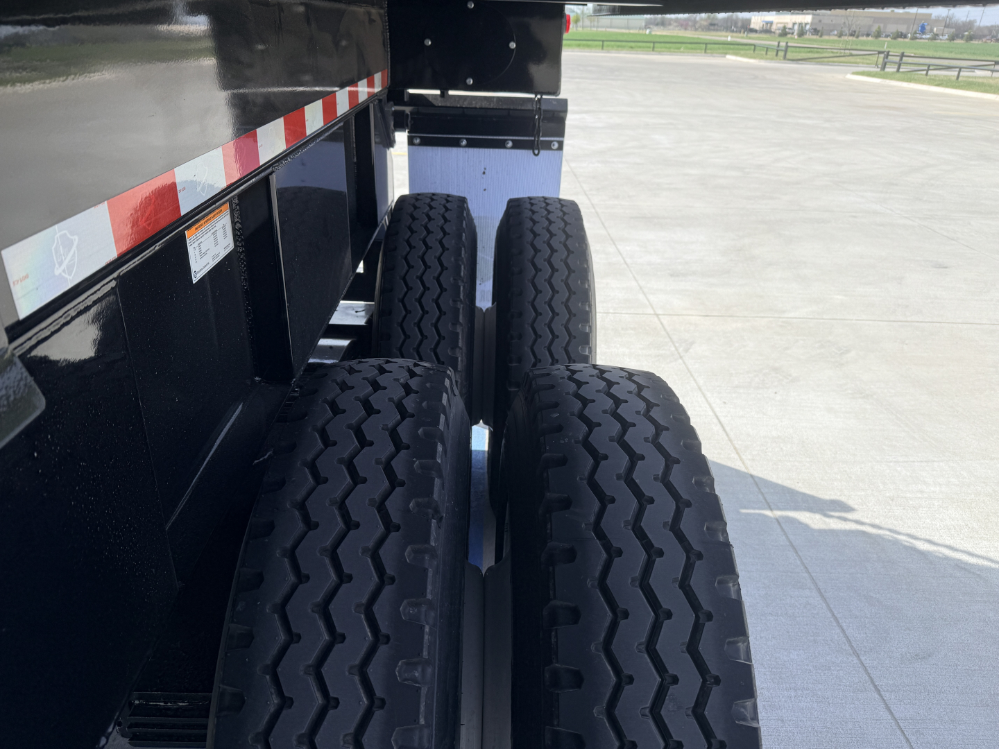 Dump trailer rear wheels view showing dual tandem axle tires and black steel frame with reflective tape.