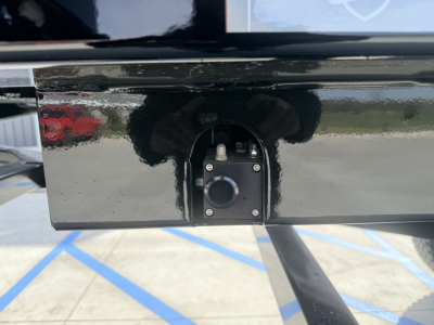 Dump trailer hitch area showing a small circular plug and mounting screws on a glossy black surface.