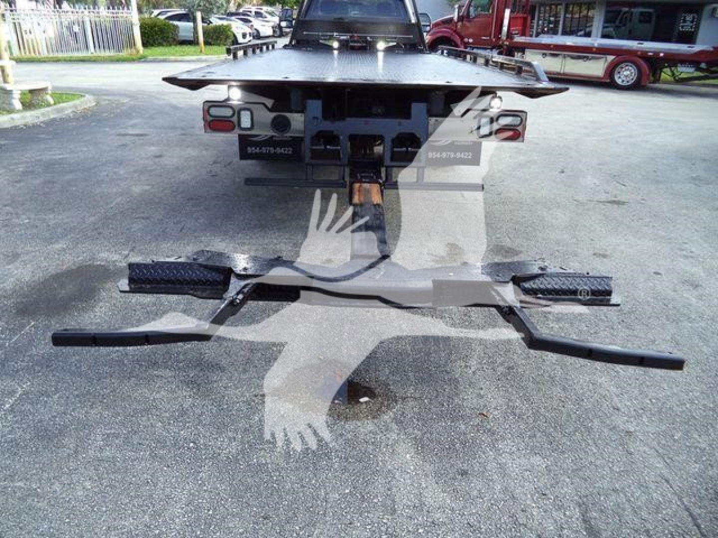 Rear view of a rollback tow truck with a hitch assembly and taillights visible; no legible labels or specifications readable on the image.