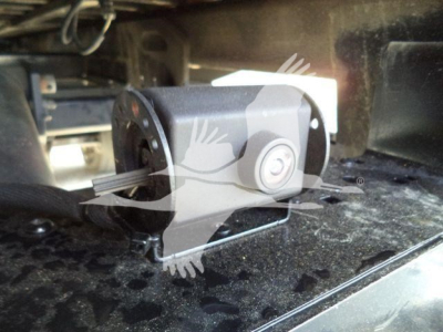 Truck rear underbody showing a camera or sensor mounting with a bracket and wiring harness; welded metal surface and a cylindrical device.