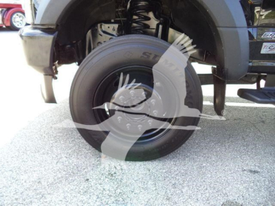 Truck wheel and suspension view of a 2022 Ford F600 rollback truck showing front left tire and wheel, partial fender, and suspension components.