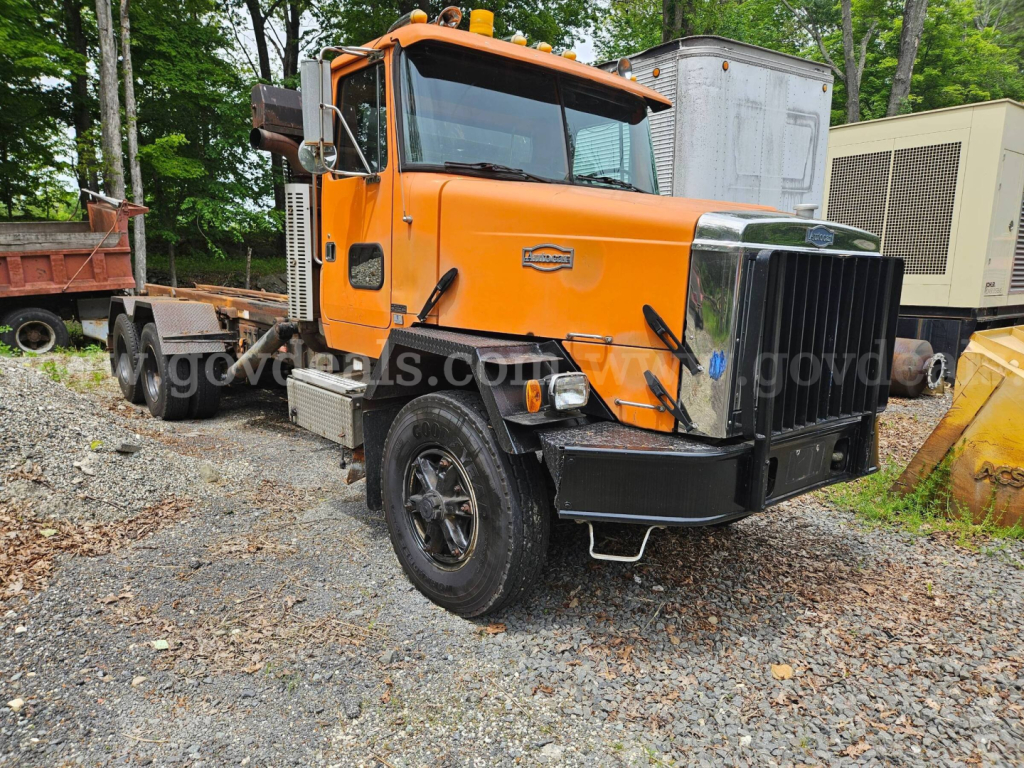 Orange 1990 Autocar ACL dump truck in a gravel lot showing front grille, cab, and heavy-duty bumper.