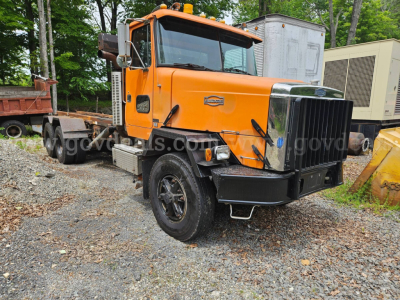 Orange 1990 Autocar ACL dump truck in a gravel lot showing front grille, cab, and heavy-duty bumper.