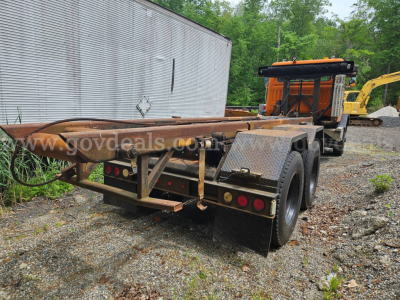 Autocar ACL roll-off truck trailer rear view showing dual rear axles and rust-toned metal frame with long flatbed; visible stock number and VIN in listing.