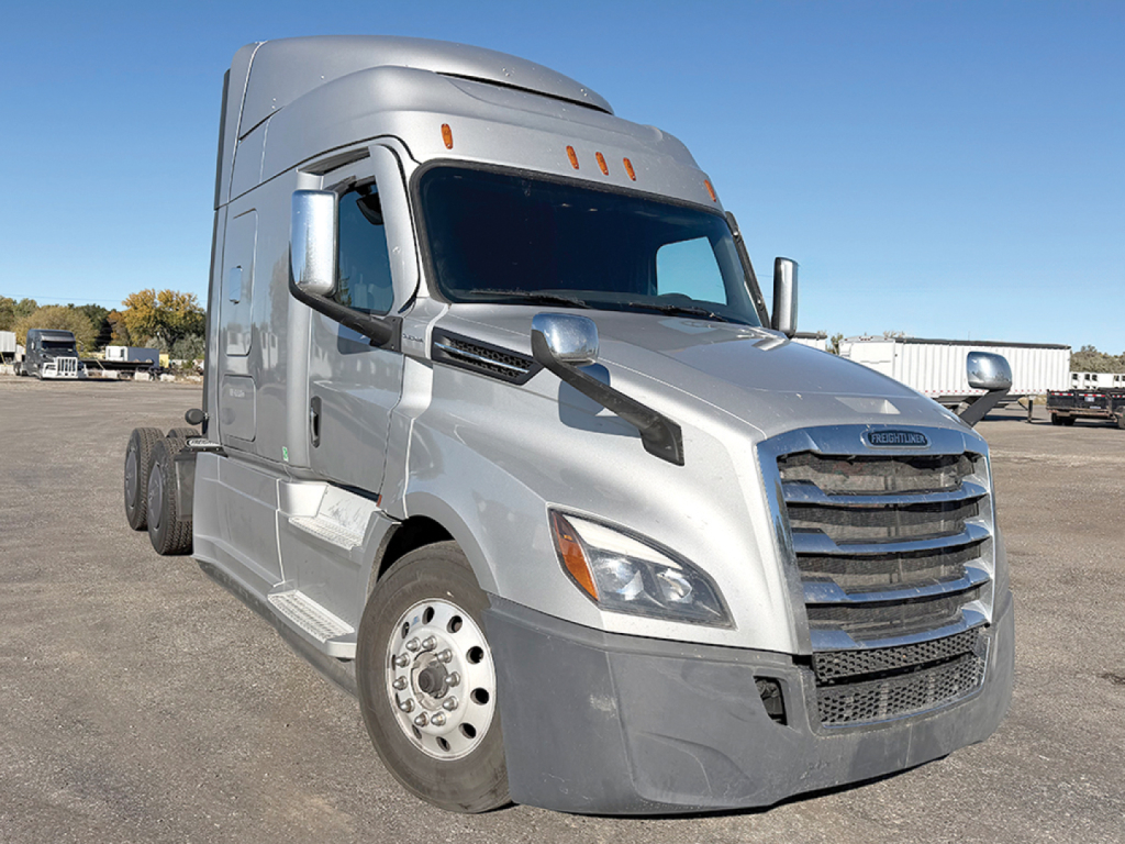 Freightliner Cascadia126 truck in a lot showing front and left side, silver color, aerodynamic mirrors, chrome grille, large sleeper cab.