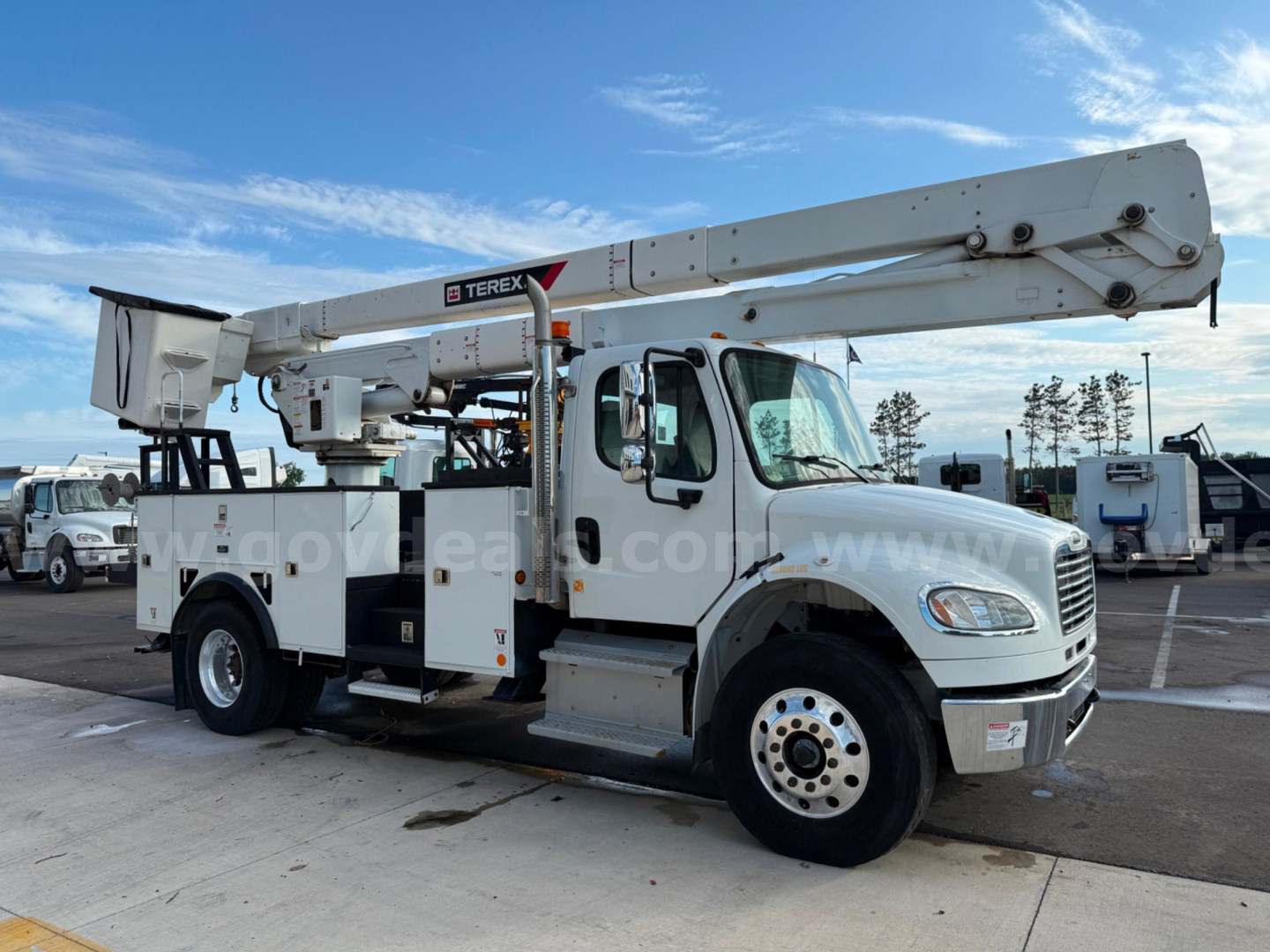Truck-mounted bucket crane on Freightliner Terex TC-55 with aerial boom extended, service compartments, and bucket at rear.