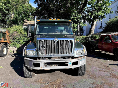 Front view of a 2005 International WorkStar 7400 dump truck showing large vertical grille, two headlights, and bumper; appears used with trees and vehicles in background.