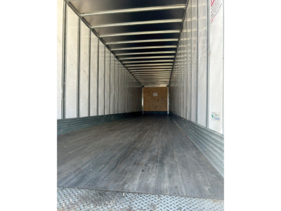Trailer interior view showing empty cargo space with metal walls, ribbed ceiling, and wooden rear door.