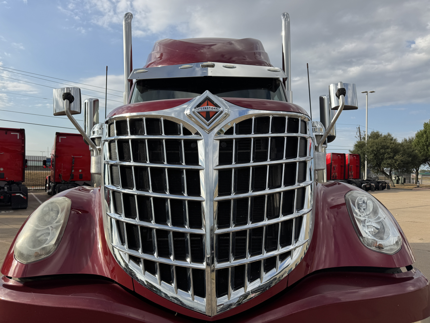 Truck grille close-up showing large chrome grille, International emblem, maroon cab, headlights visible on sides.