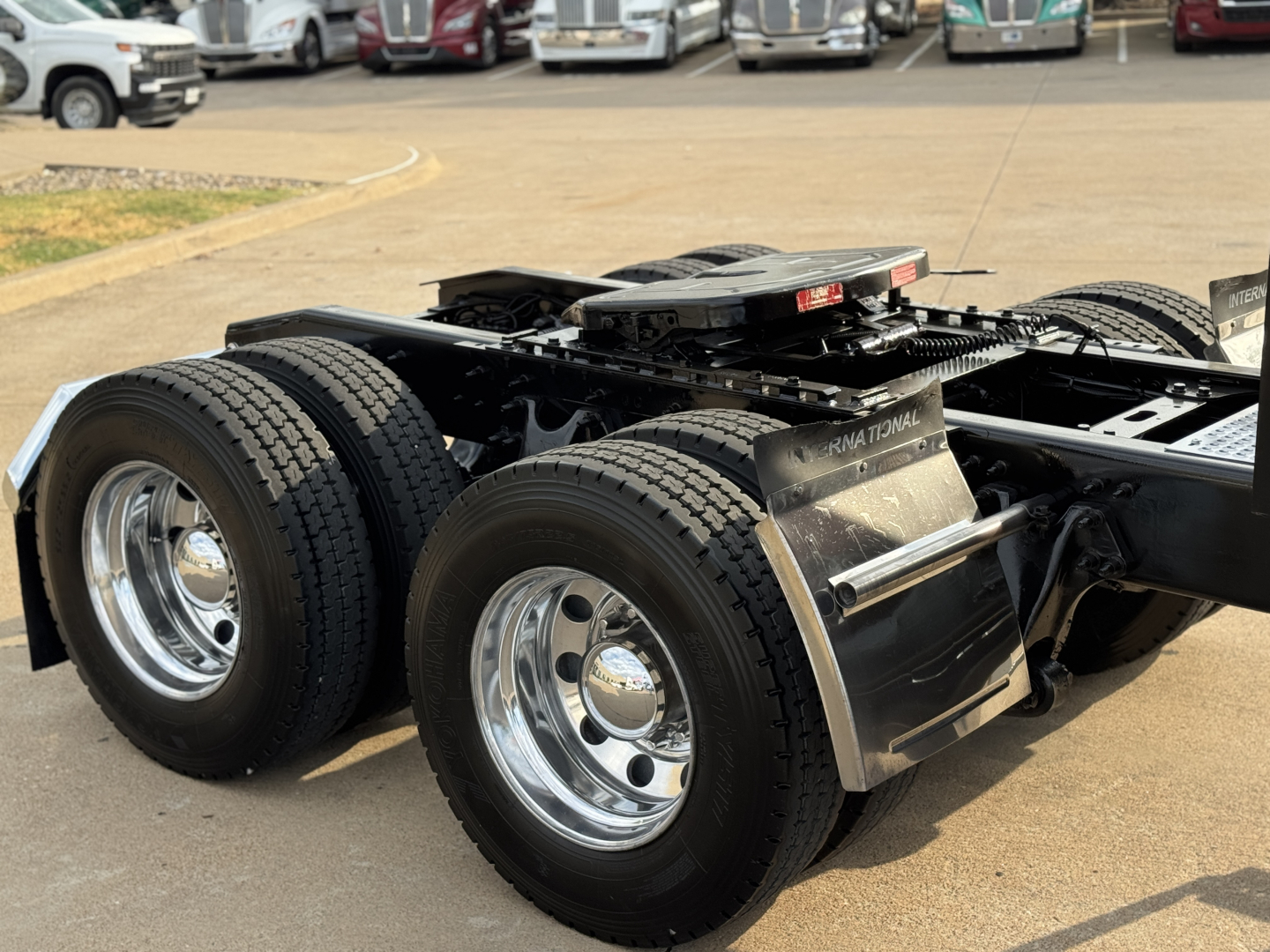 Truck chassis showing rear dual-axle configuration with large black tires and polished chrome wheels; partial fenders and fifth-wheel mount visible; International Lonestar branding on mudguard.