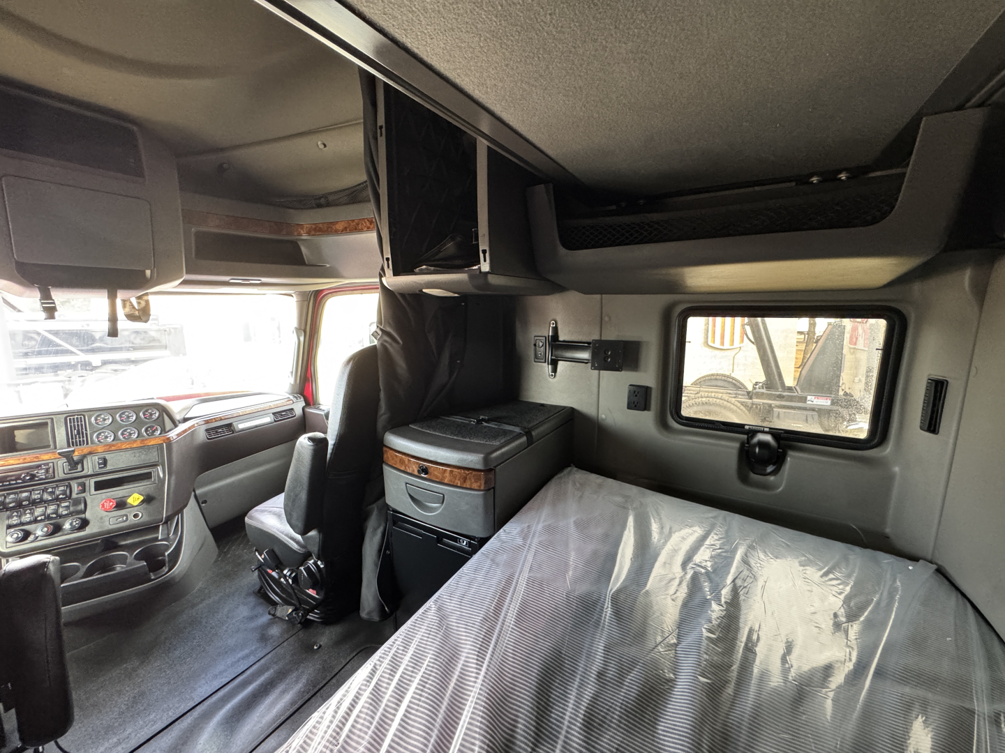 Cab interior of a 2021 International Lonestar sleeper showing front dash, overhead storage, and a bed with plastic cover.
