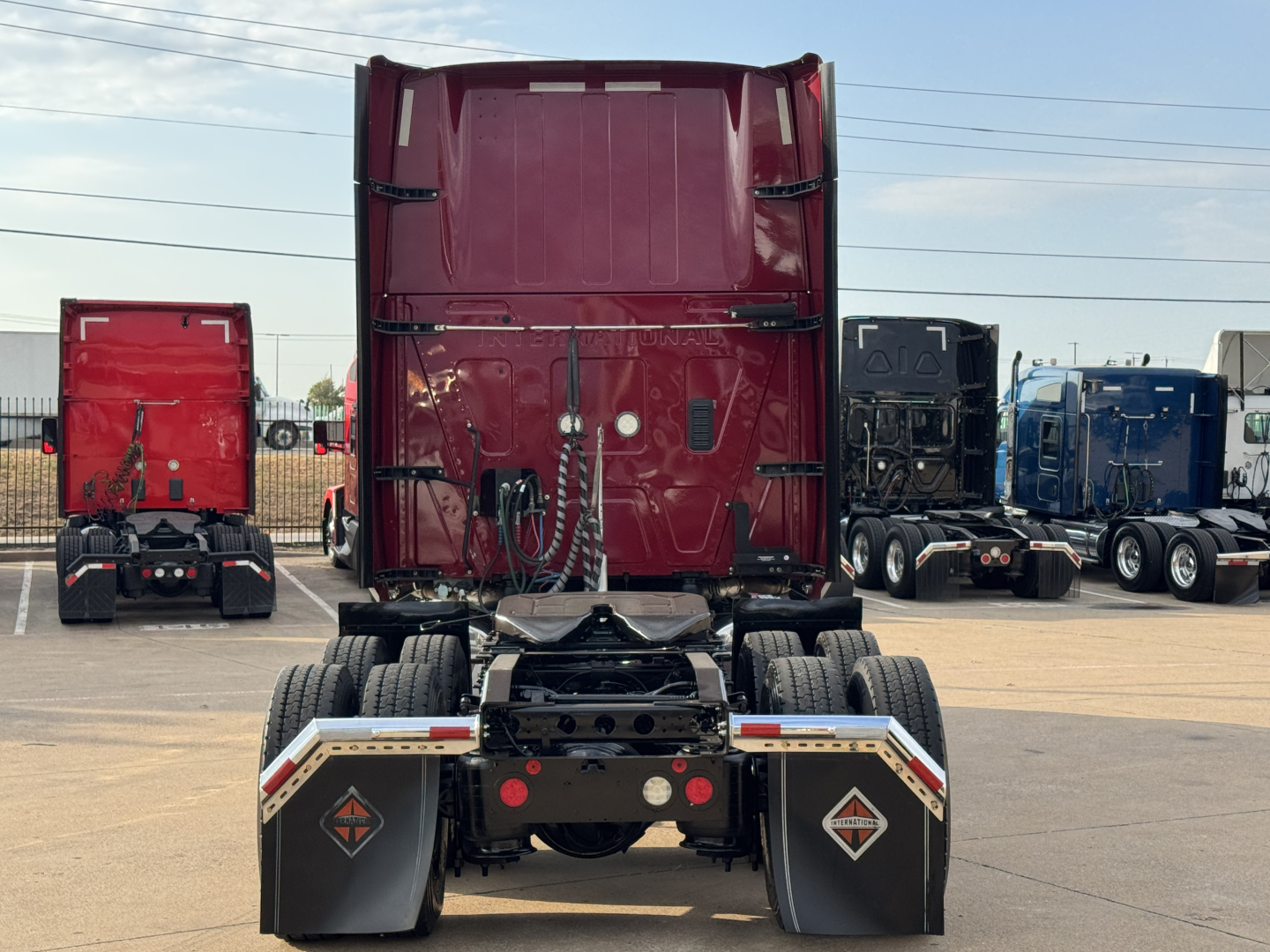 Truck chassis with fifth wheel, rear view showing dual rear axles, mud flaps with logos, and tail area of a red sleeper truck.
