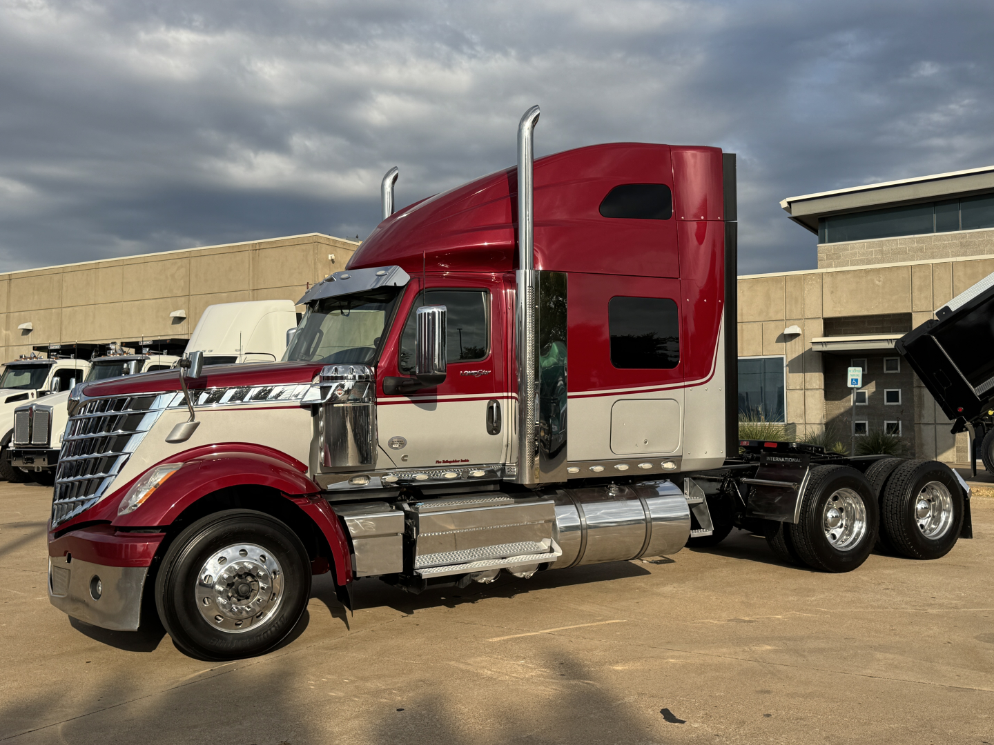 Side view of a red and beige 2021 International Lonestar heavy truck, sleeper cab, chrome exhaust stacks, dual rear axles, with a dump bed visible on a trailer.