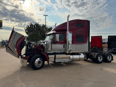 Truck cab side view showing red and white 2021 International Lonestar with hood open, exposed engine area, large chrome fuel tanks, and dual rear axles.