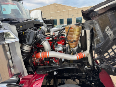 Engine bay of a 2021 International Lonestar sleeper showing a red engine with hoses, coolant reservoir, and surrounding components.