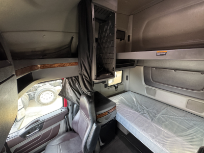 Interior sleeper cab of a 2021 International Lonestar truck showing bunk bed with mattress, overhead storage, and mesh partition, driver seat area visible.