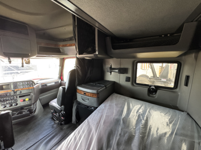 Cab interior of a 2021 International Lonestar sleeper showing front dash, overhead storage, and a bed with plastic cover.