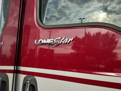 Truck door badge reading LONESTAR on a red International truck with reflection of sky; chrome script logo shows Lonestar emblem.