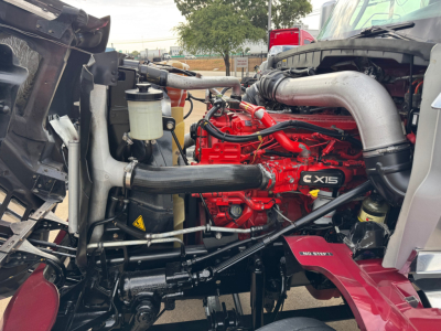 Truck engine bay of a 2021 International Lonestar showing red engine block with X15 badge, silver intake pipe, black hoses, and auxiliary components.