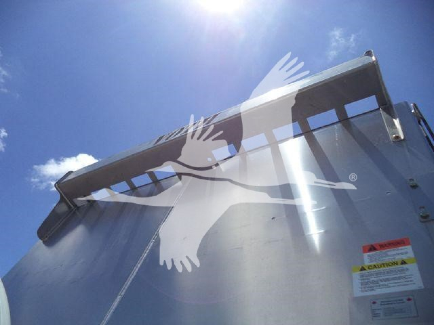 Dump truck bed side and tailgate of a 2023 Chevrolet Silverado 6500HD with a warning sticker visible and a reflection of a bright sky.