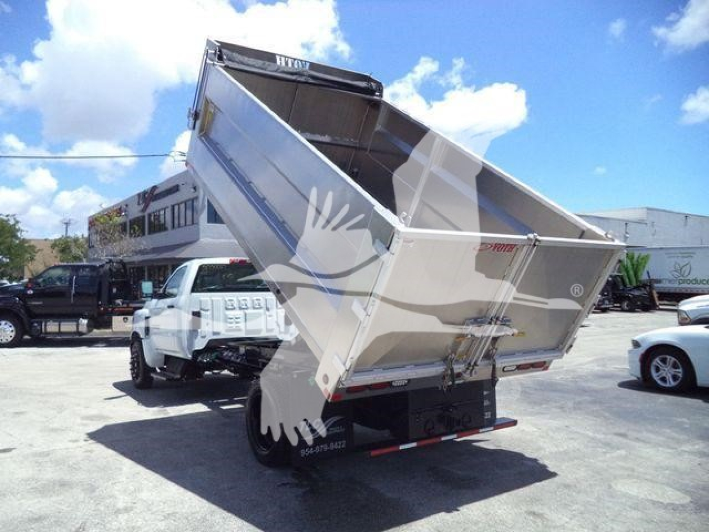 Chevrolet Silverado 6500HD dump truck bed raised showing aluminum dump body and tailgate with stickers and wheelbase in a dealership lot.