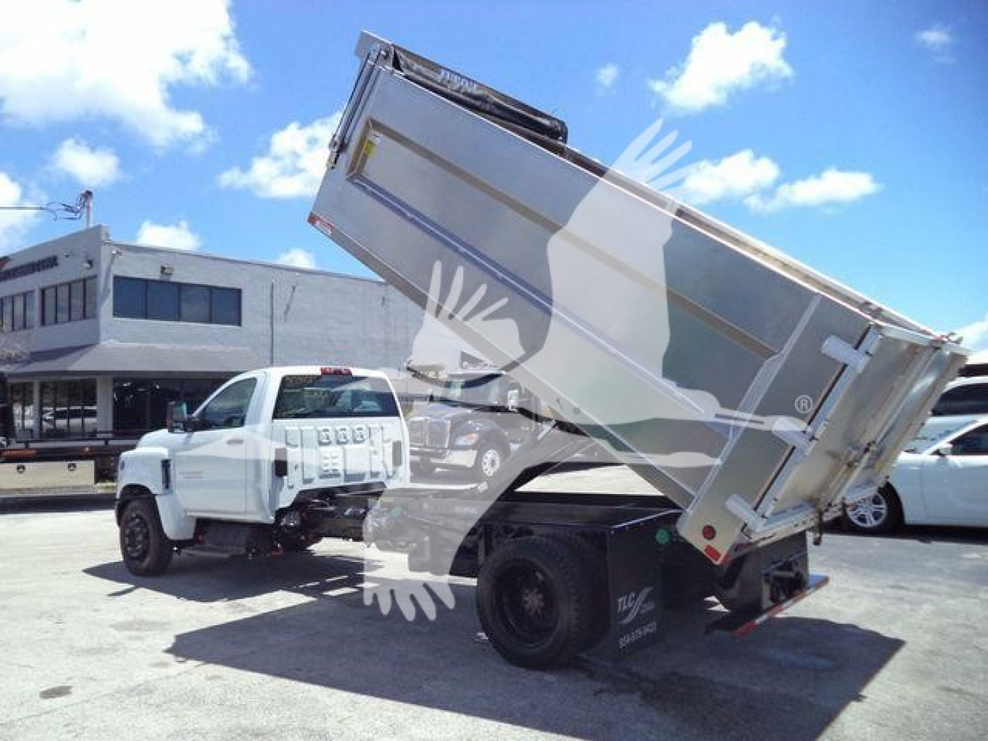 Dump truck bed tilted with Chevrolet Silverado 6500HD chassis, aluminum dump body, forward cab, stock photo at dealership lot.