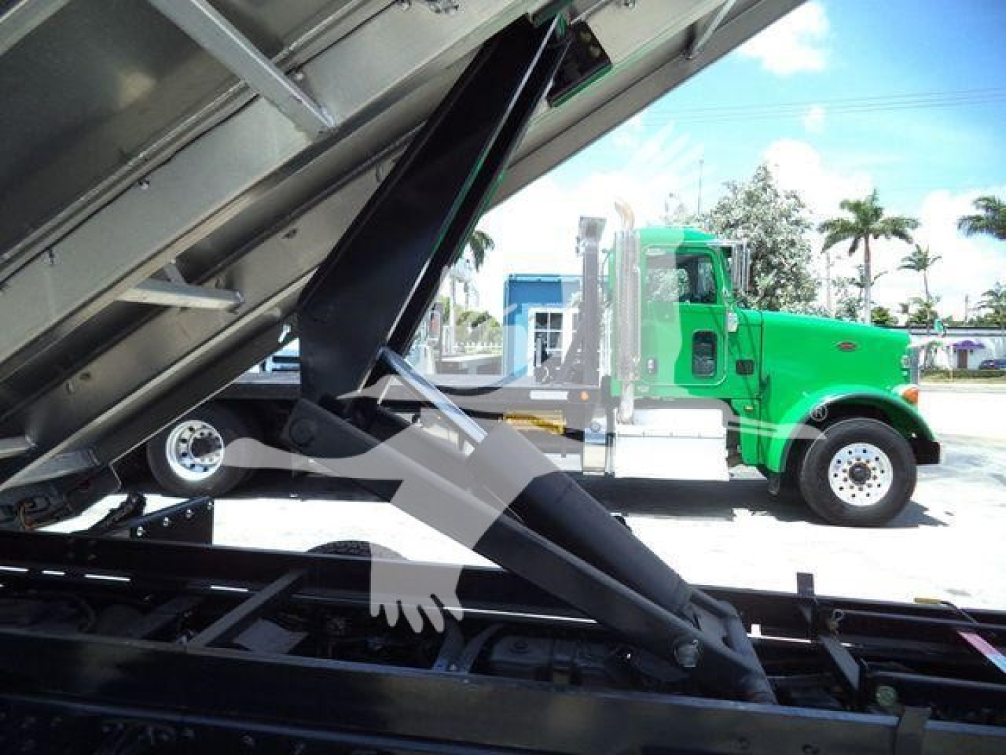 Truck bed of a Chevrolet Silverado 6500HD in a dump configuration with hydraulic lift arms and green cab visible in background.