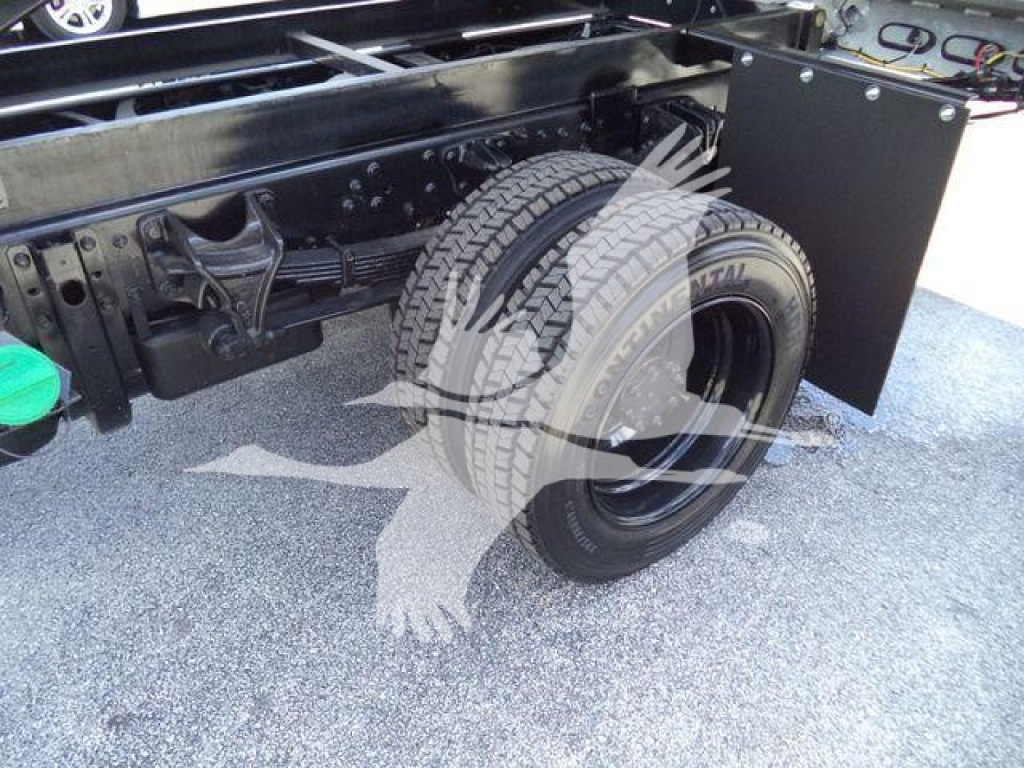 Truck chassis with rear dual wheels, frame rails, and dump bed area visible; wheel and suspension components, fuel/fluids area, and a black toolbox mounted near the cab.