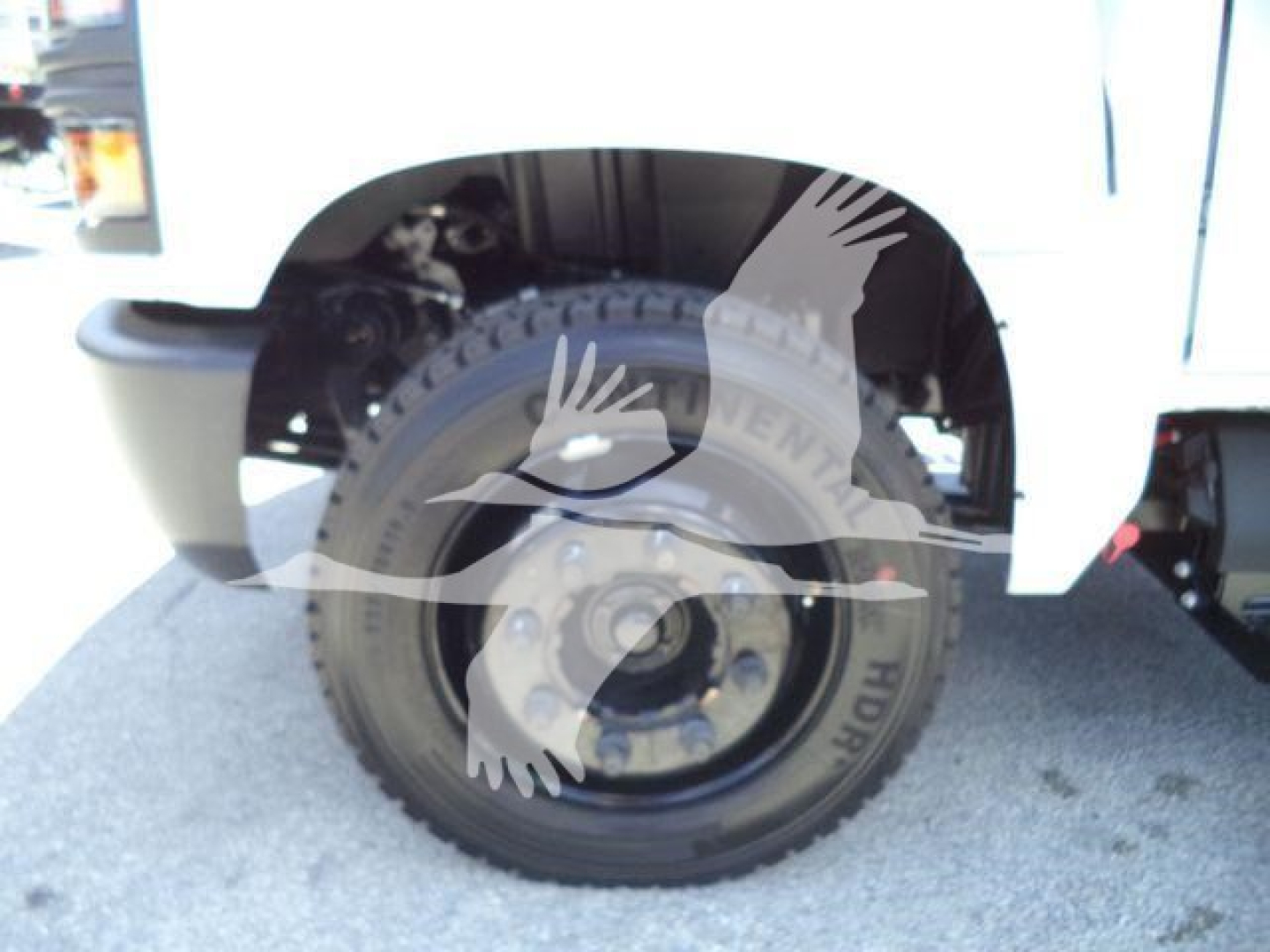 Truck wheel well and front tire of a 2023 Chevrolet Silverado 6500HD dump truck showing steel wheels and heavy-duty tire.