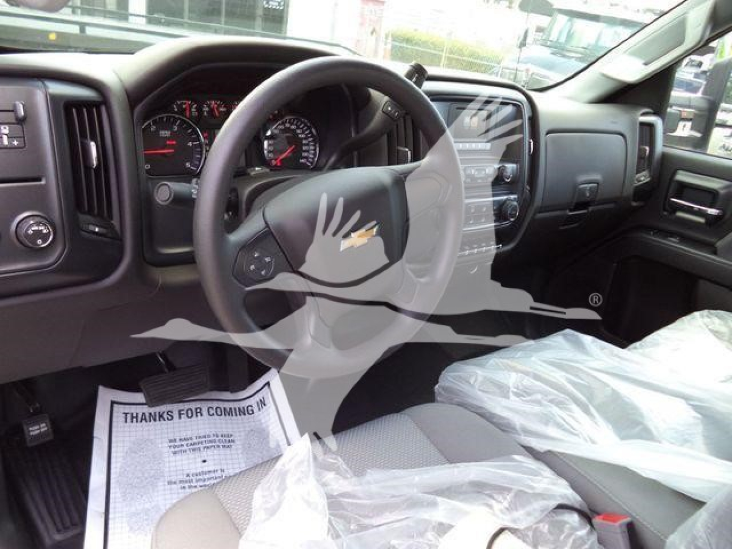 Interior of 2023 Chevrolet Silverado 6500HD dump truck showing steering wheel, dashboard, and front seats; plastic seat cover and floor mat with paperwork visible.