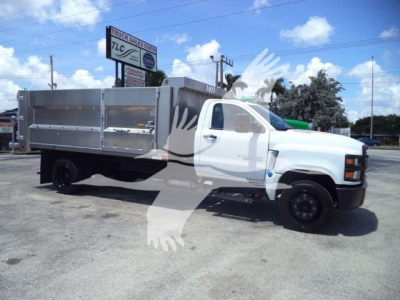 Truck shows 2023 Chevrolet Silverado 6500HD dump body with aluminum dump bed, side panels, and standard cab. Visible signage includes a TLC dealership sign in background.