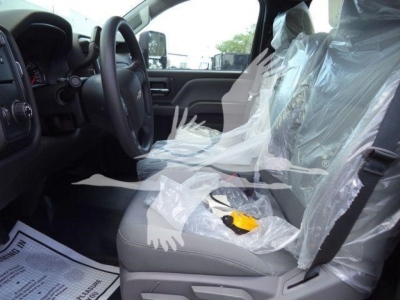 Chevrolet Silverado 6500HD interior view showing plastic-wrapped front seats and steering wheel, with plastic seat covers and a yellow tool on the front seat.