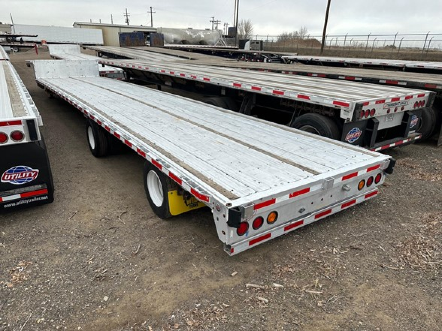 Flatbed trailer showing all-aluminum air ride drop deck with multiple tandem axles and reflective safety tape along the sides.