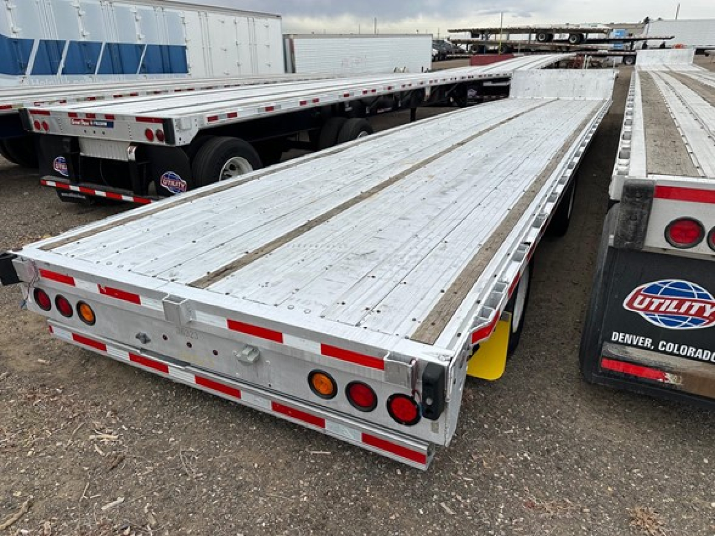 Flatbed trailer deck with aluminum structure and drop deck design, rear view showing taillights, reflective tape, and tandem axles.