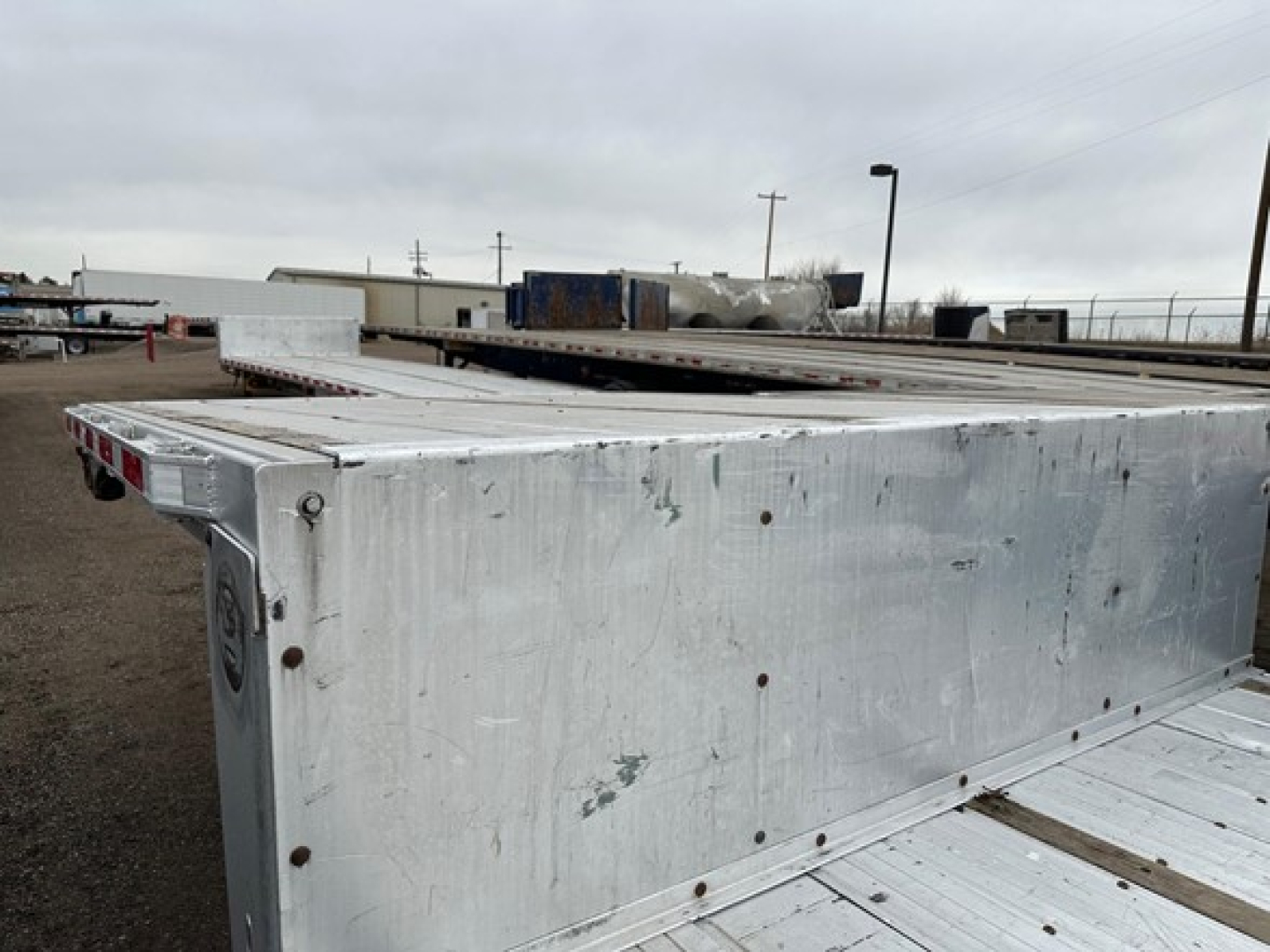 Aluminum drop deck trailer side view showing riveted aluminum surface with screws along edge and a circular recessed area near corner.