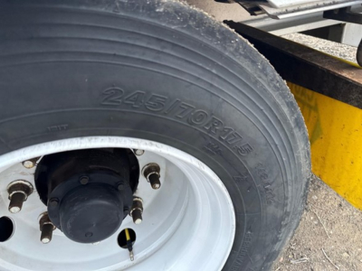 Trailer wheel and tire close-up showing 245/70R19.5 tire on a white rim, with hub and lug nuts visible.