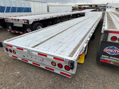Flatbed trailer deck with aluminum structure and drop deck design, rear view showing taillights, reflective tape, and tandem axles.